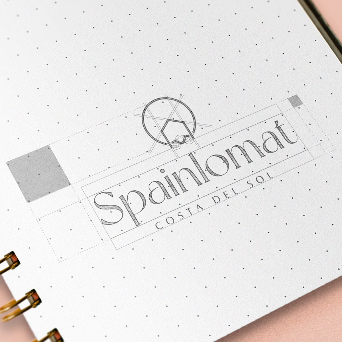 Logo construction sketch on dotted paper: the Spainlomat wordmark and mark with alignment guides.